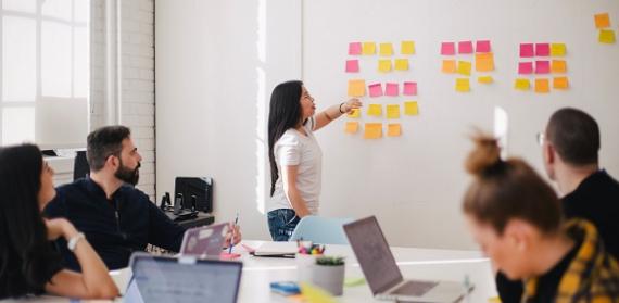 Employee pointing out to post-its on the wall during a meeting with colleagues